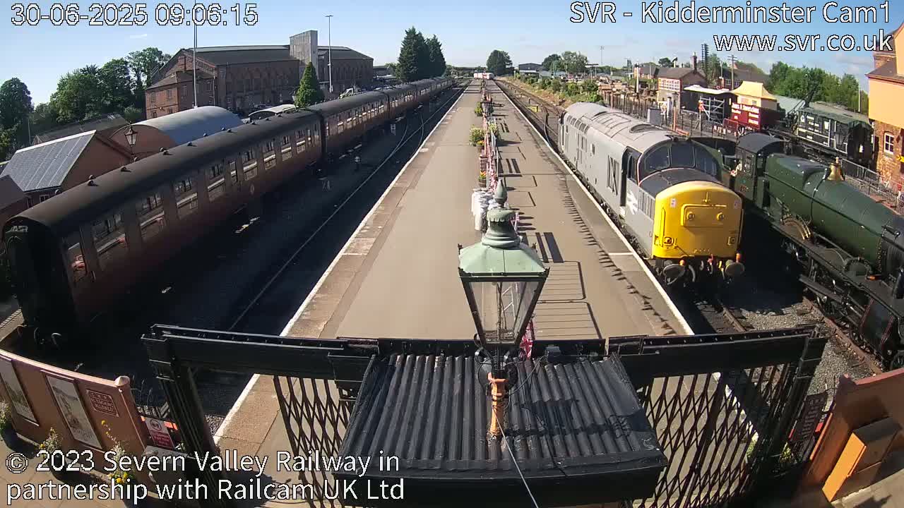 Multiple passenger trains and locomotives are parked at a sunny railway station.