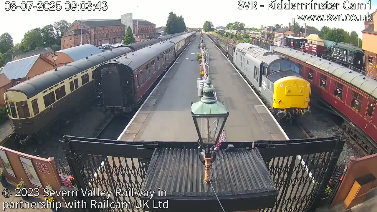 Several vintage passenger train cars and locomotives are parked on railway tracks on a sunny day.
