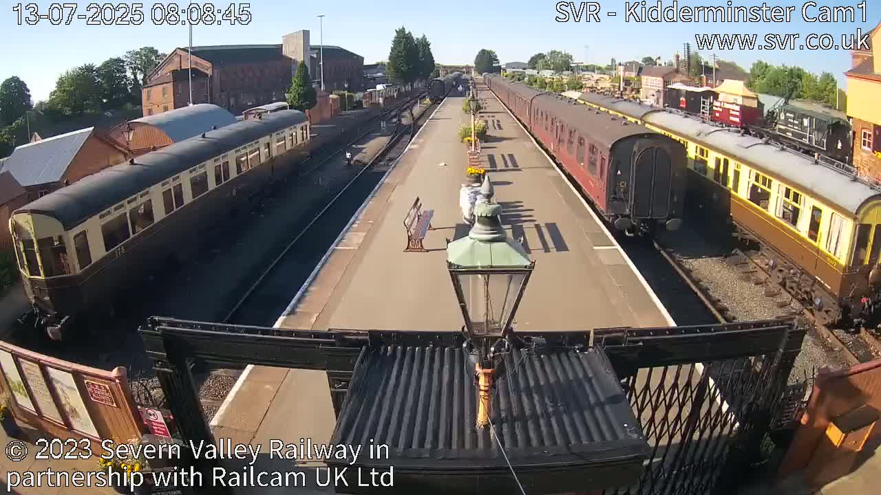 Two vintage passenger train cars are parked at a railway station on a sunny day.