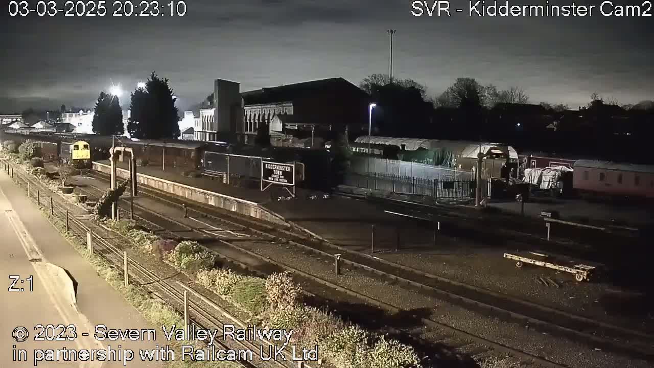 A nighttime view of a train station with several train cars and locomotives on the tracks under a dark, overcast sky.