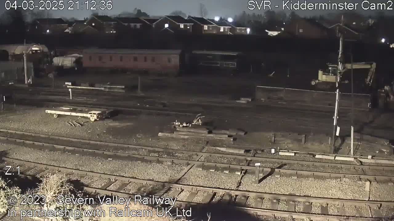 A nighttime view of a railway yard with several train cars, a flatbed railcar, and some construction equipment.