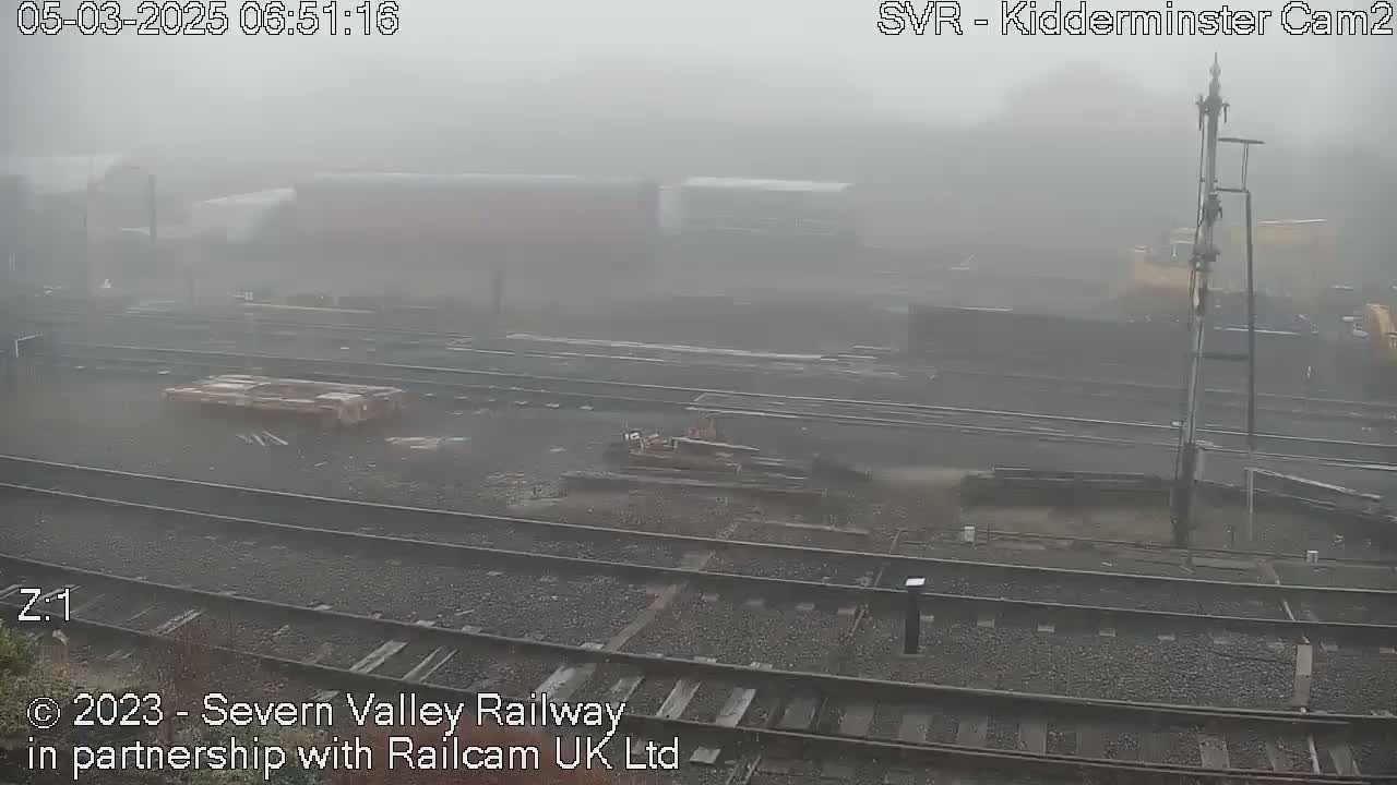 A foggy view of a railway yard with several train cars and tracks visible in the distance.