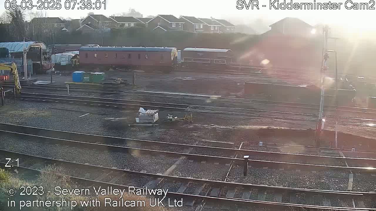 A sunny morning reveals several railway carriages parked in a yard with multiple sets of train tracks.