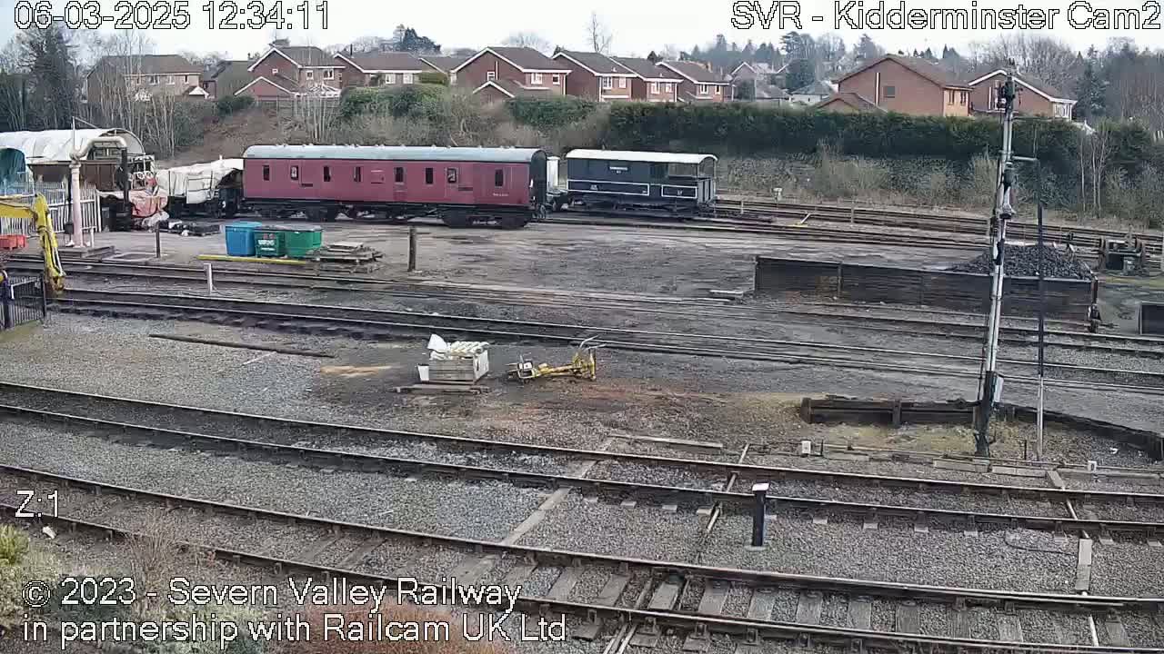 Several railway cars sit on a track in an overcast outdoor setting near residential buildings.