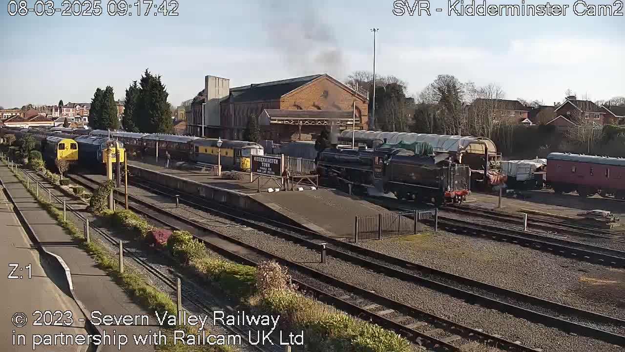 A steam train and several other railway cars are parked at a train station on a sunny day.