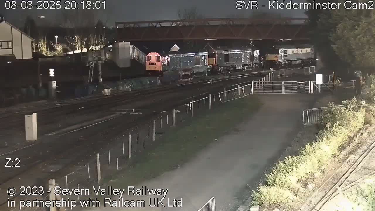 At night, several diesel locomotives are parked on a rail line near a bridge and some vegetation.