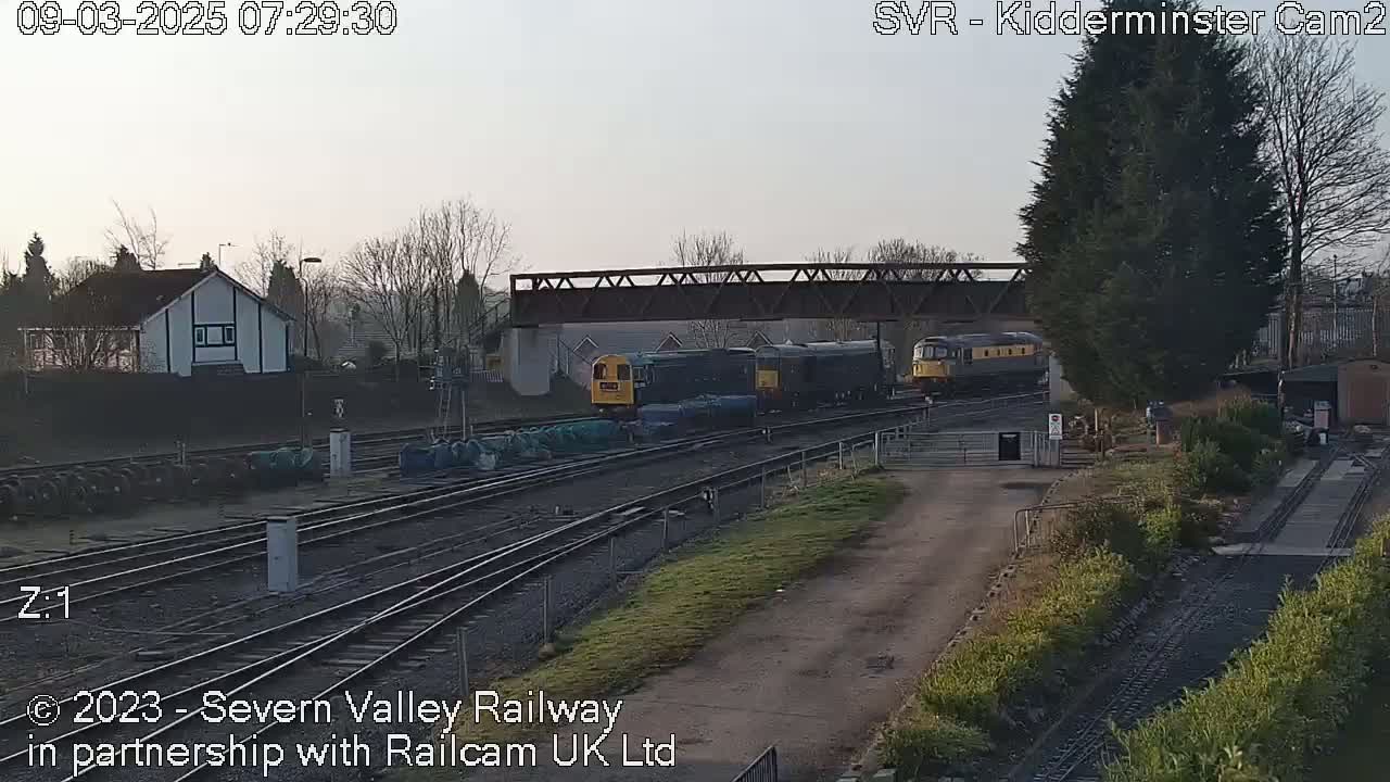 A train of several diesel locomotives sits in a railway yard on a slightly overcast morning.
