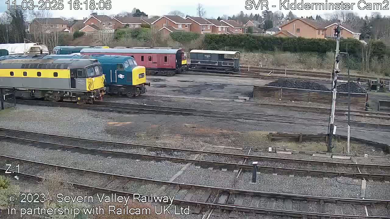Several diesel locomotives and railway carriages are parked on a railway yard under an overcast sky.