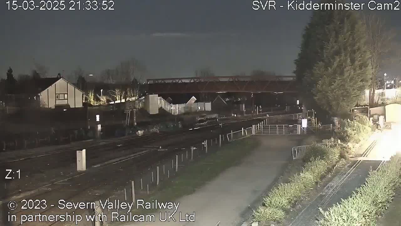 A nighttime view of train tracks, a bridge, and nearby buildings under a dark sky.