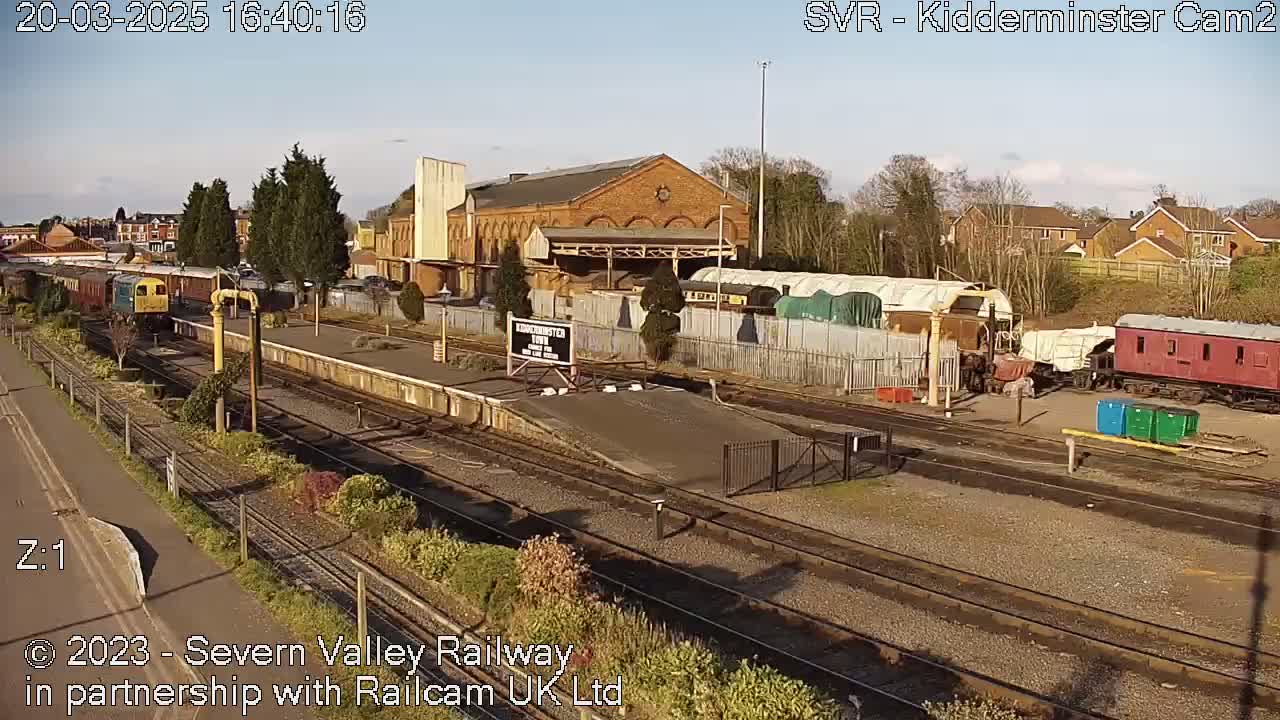 A sunny day at a train station with several railway cars and a brick building.