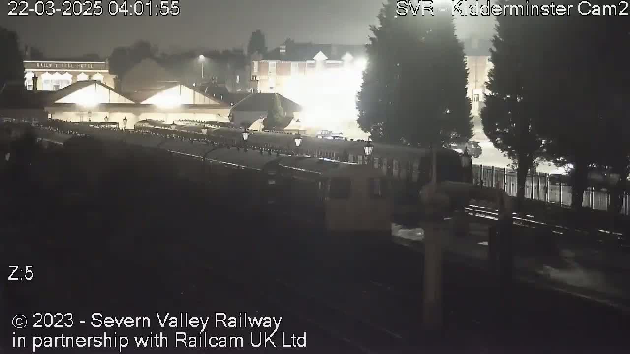A nighttime view of a train station and its surrounding buildings under hazy, dark conditions.