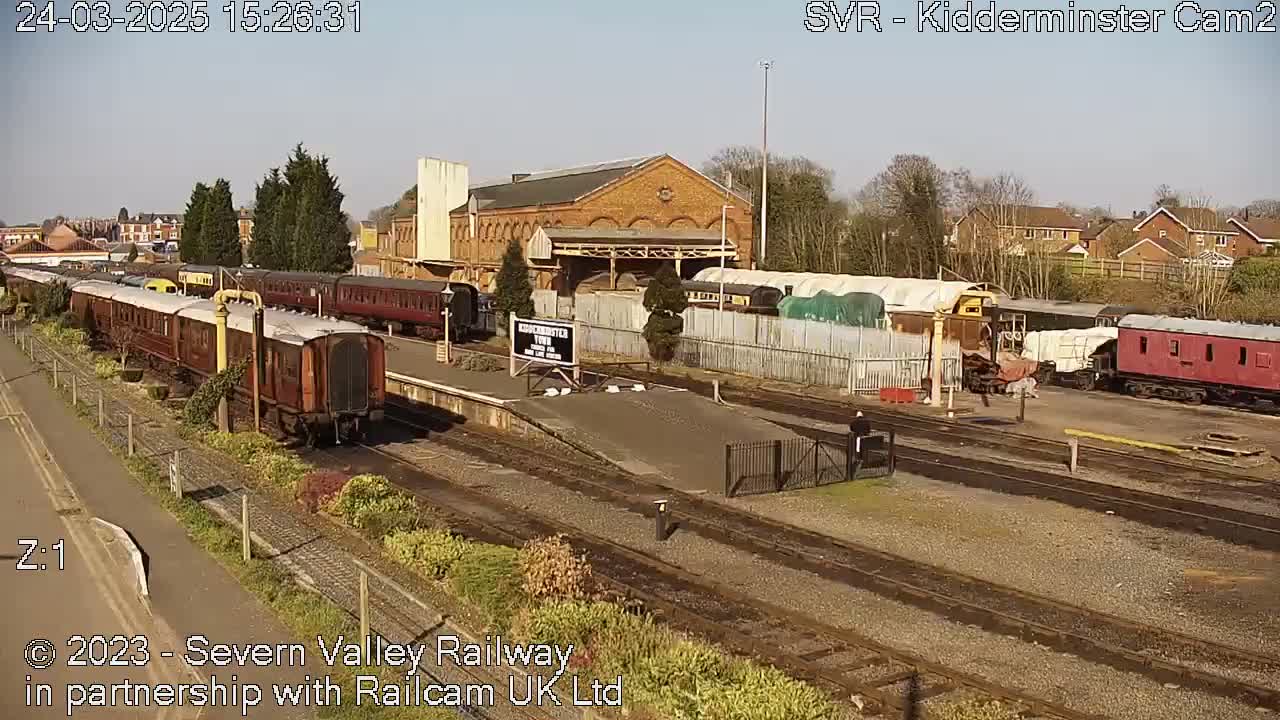 A sunny day at a train station shows multiple passenger cars and rail cars parked on tracks next to a brick building.