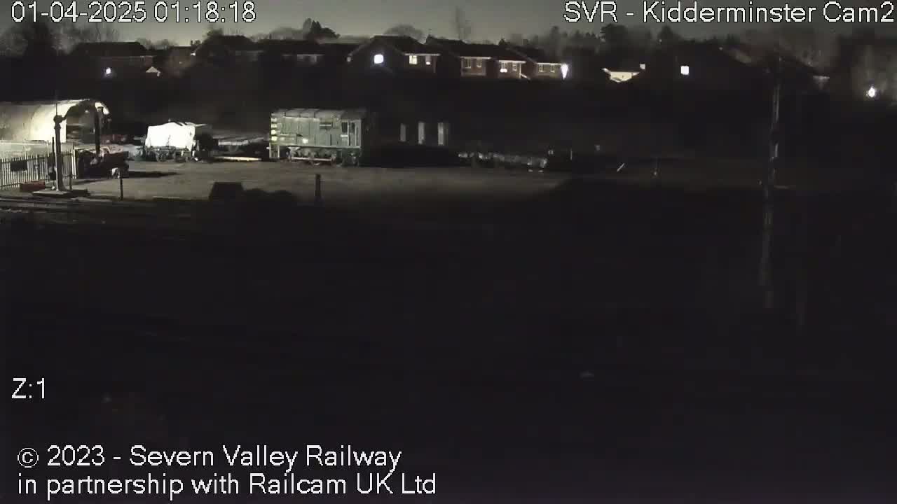 At night, several railway cars are parked in a dimly lit area next to a building.