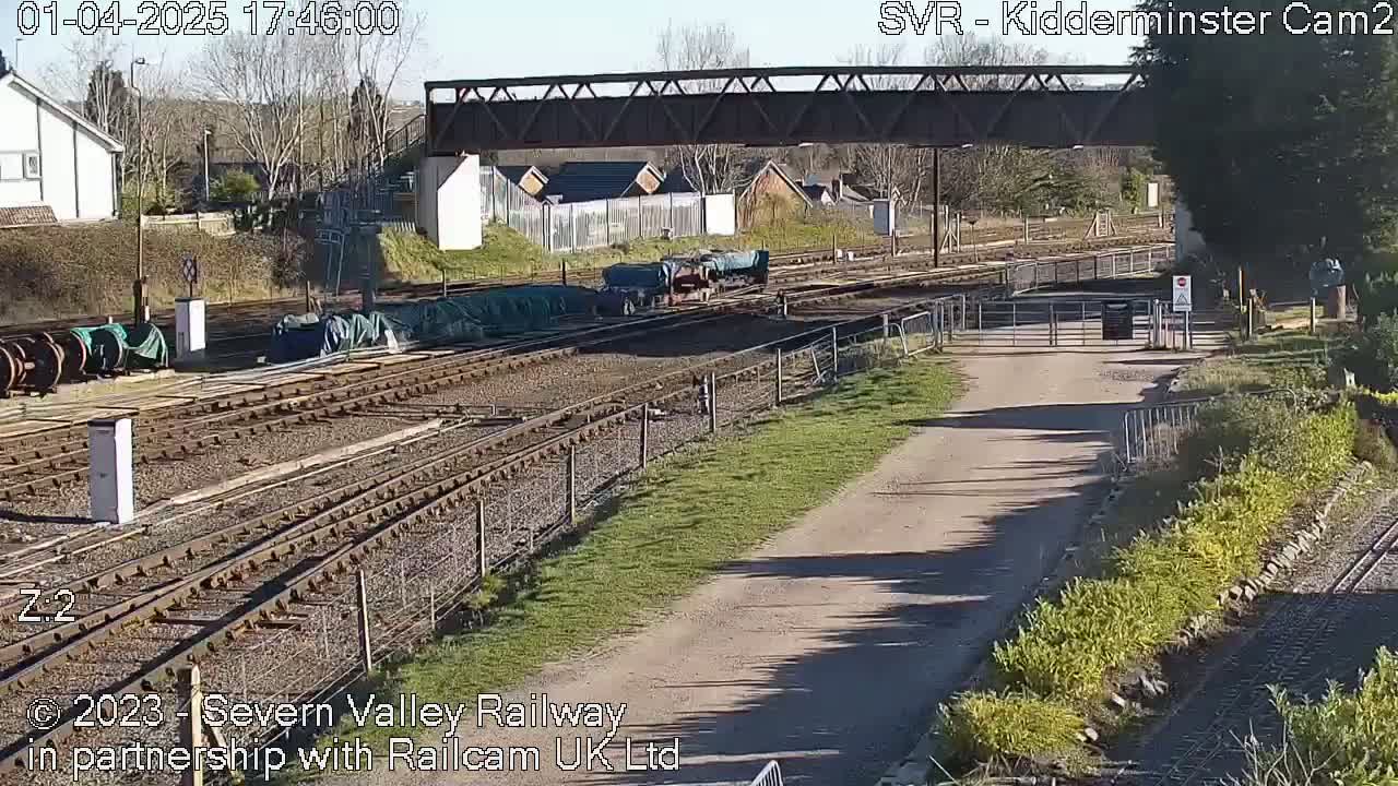 A sunny view of a railway yard with several railcars and a metal bridge overhead.