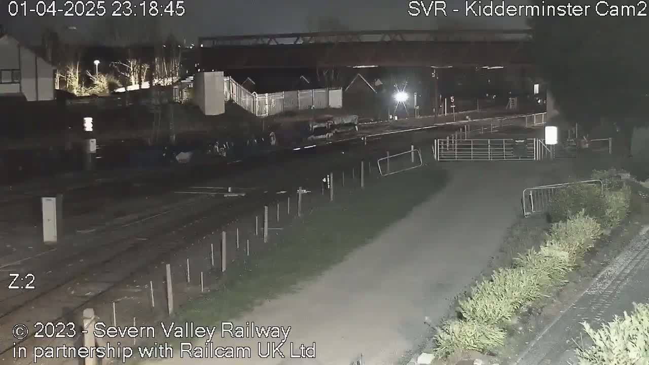 A nighttime view of a railway track and surrounding area, under dark conditions with some low-level lighting.