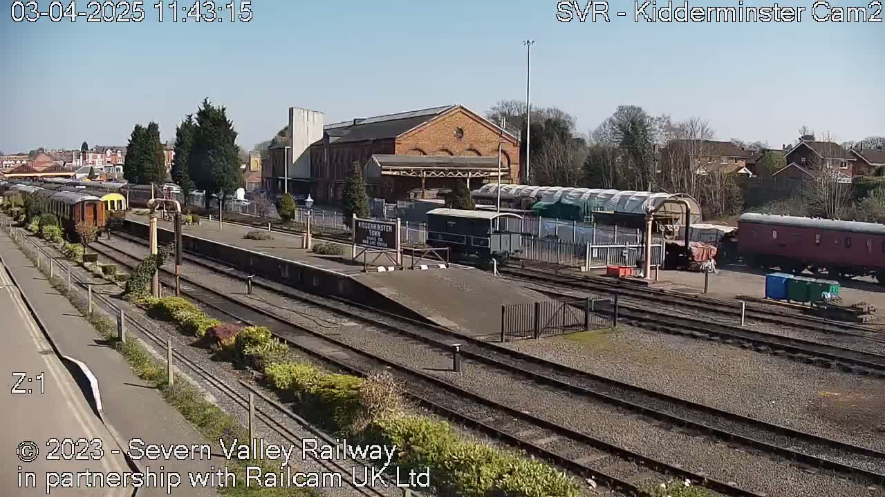 A sunny view of a train station with several railway cars and carriages on multiple tracks, under a clear blue sky.