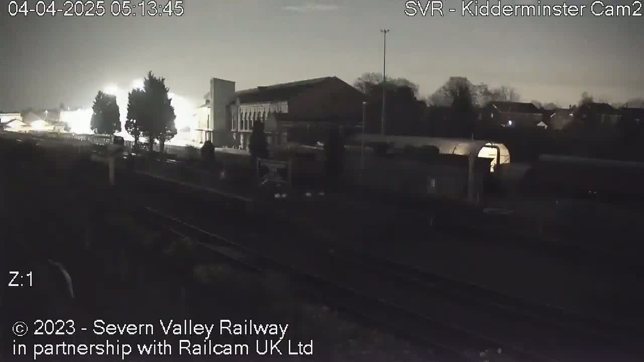 A nighttime view of a train station with a train and some buildings under a dark sky.