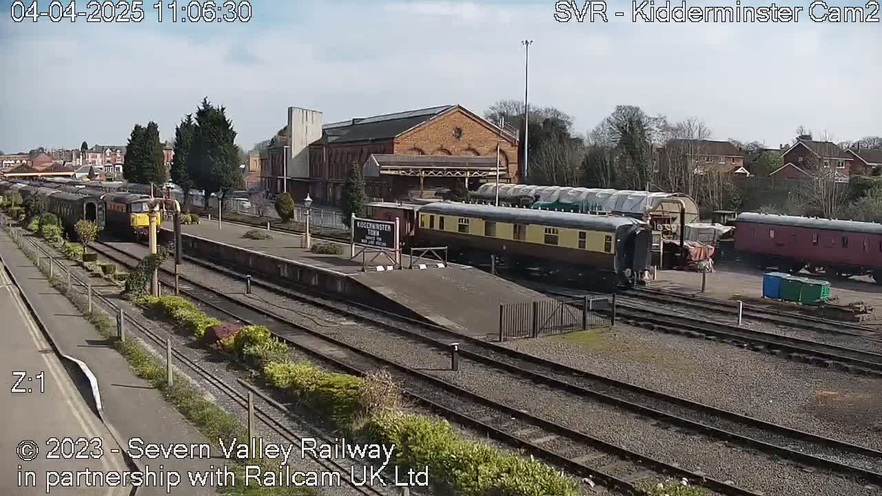 A train station with several railway cars and a diesel locomotive on a sunny day.