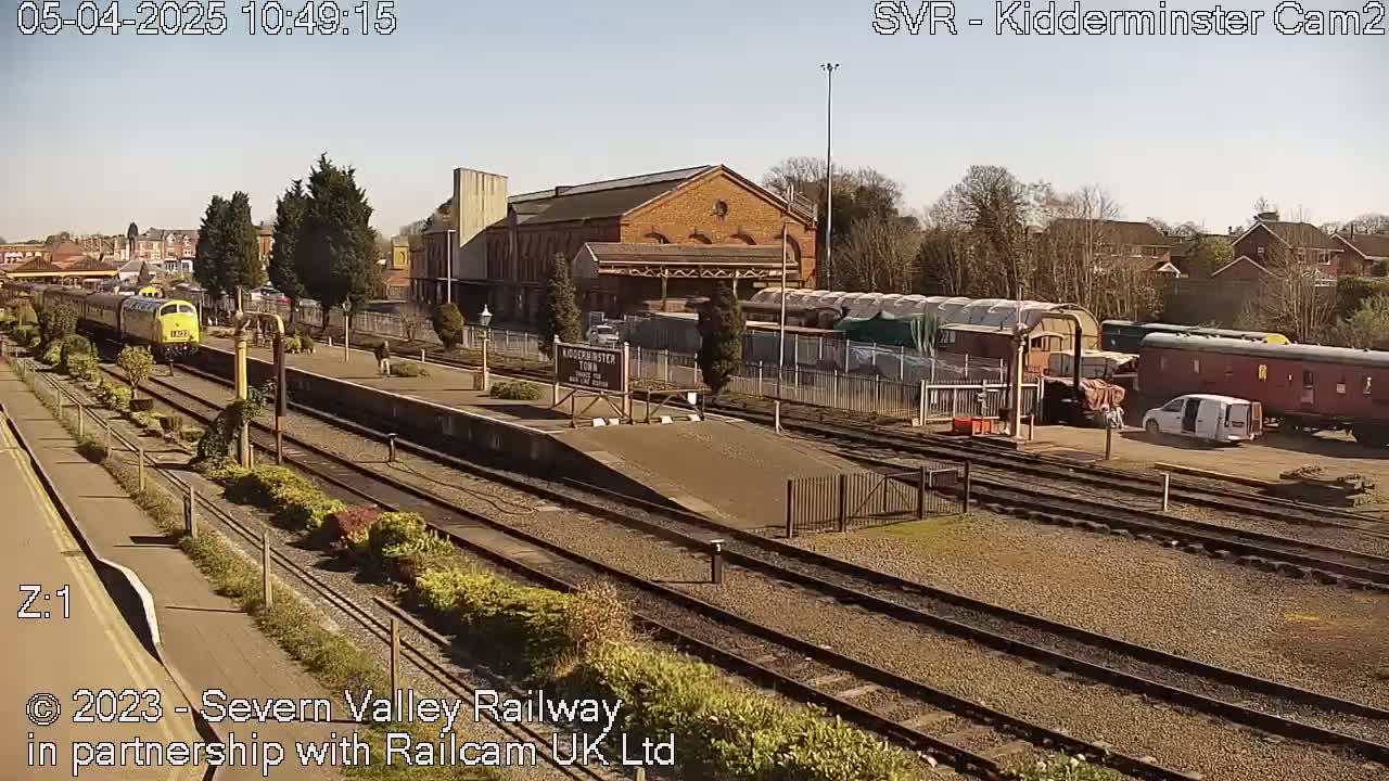 A yellow diesel train is departing from a train station on a sunny day.