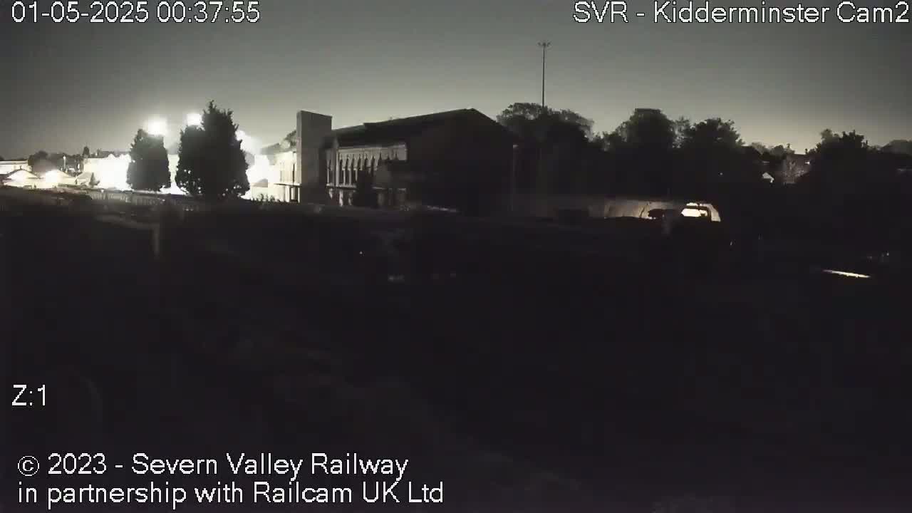A dark, nighttime scene shows a building and trees illuminated by faint lights.