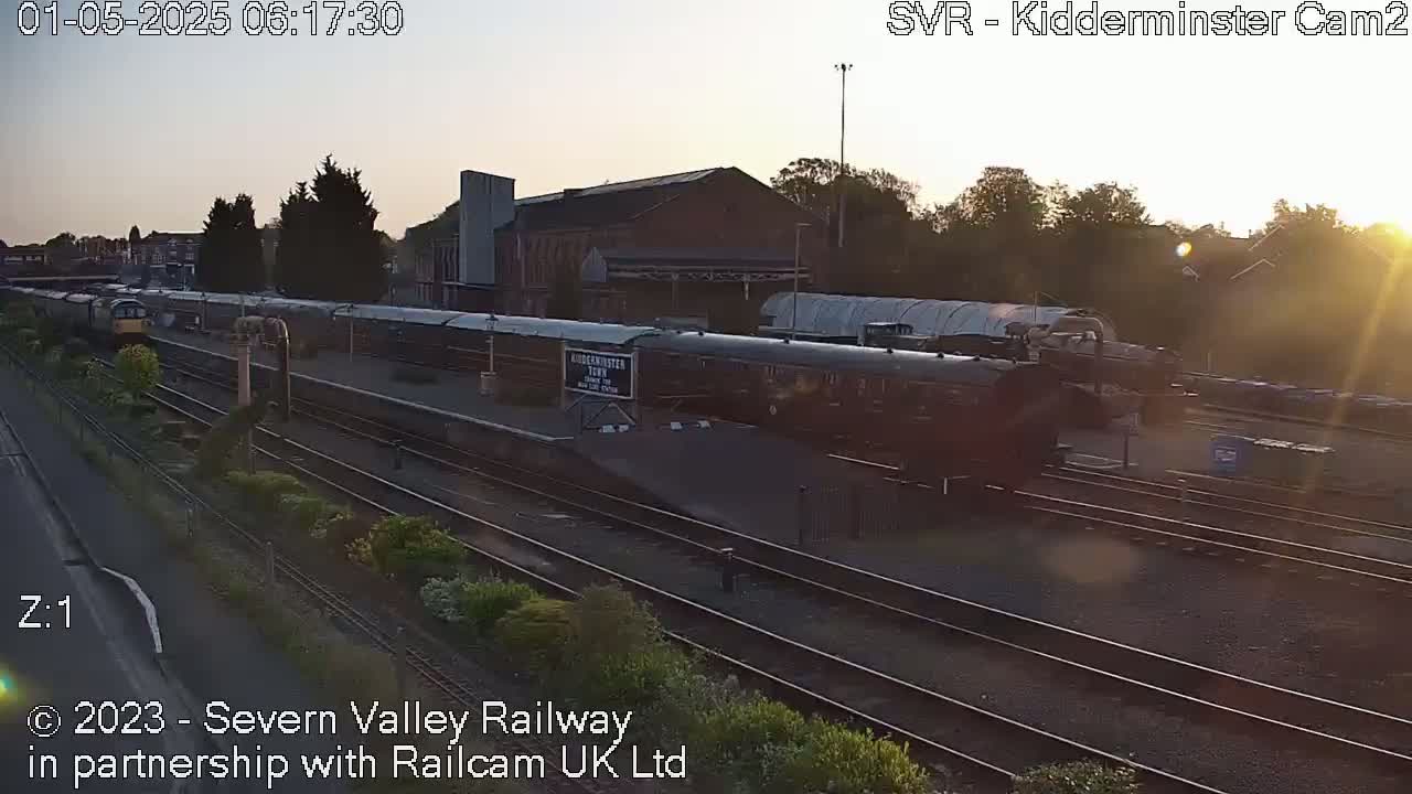 A train sits at a station platform during sunrise, under a clear sky.
