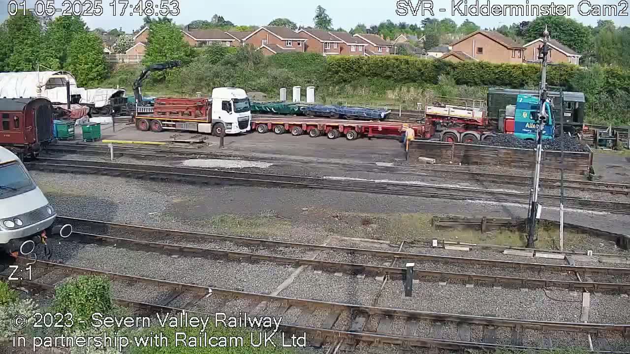 A railway yard on a partly sunny day with several railcars, a crane, and several trucks, including one carrying coal.