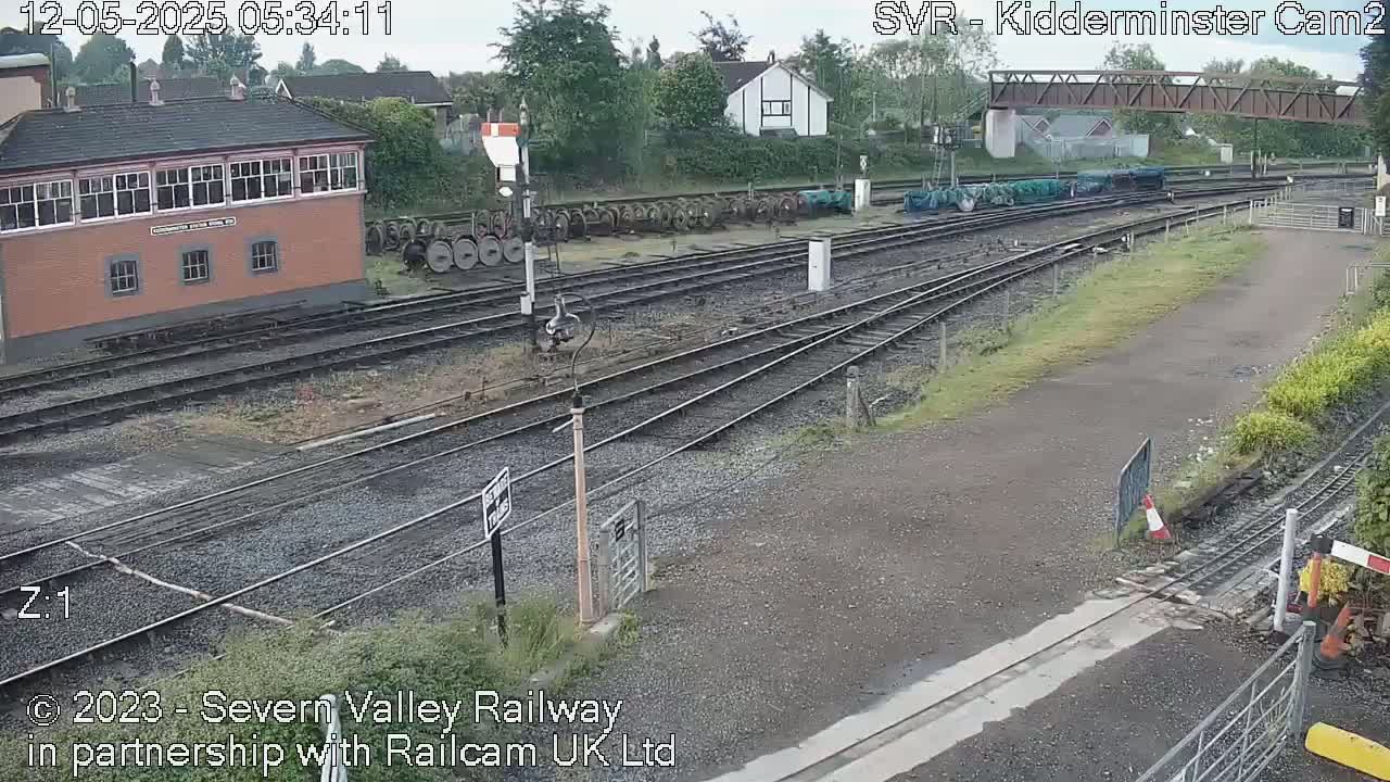 A railway yard with a signal box, several train cars, and a network of tracks under an overcast sky.
