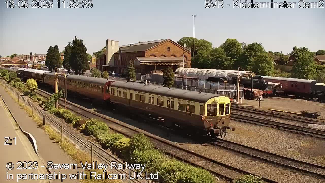 A long passenger train sits in a train station on a sunny day.