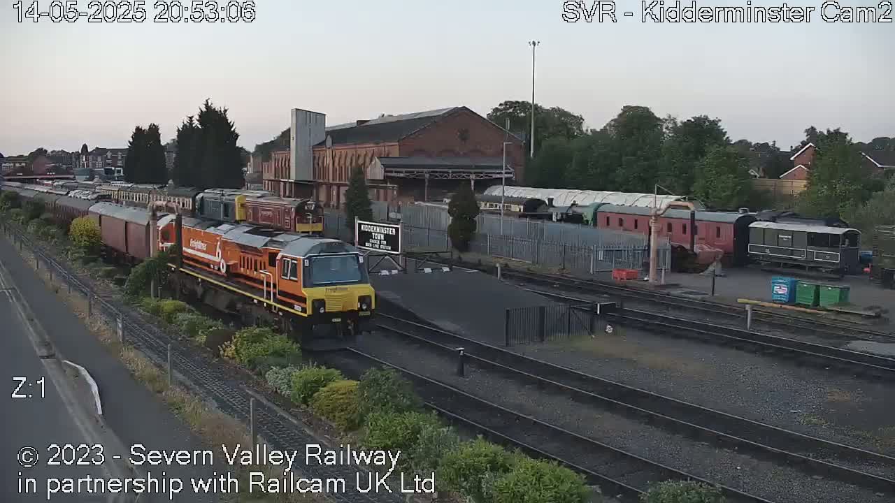 A freight train pulls into a railway station under a twilight sky.