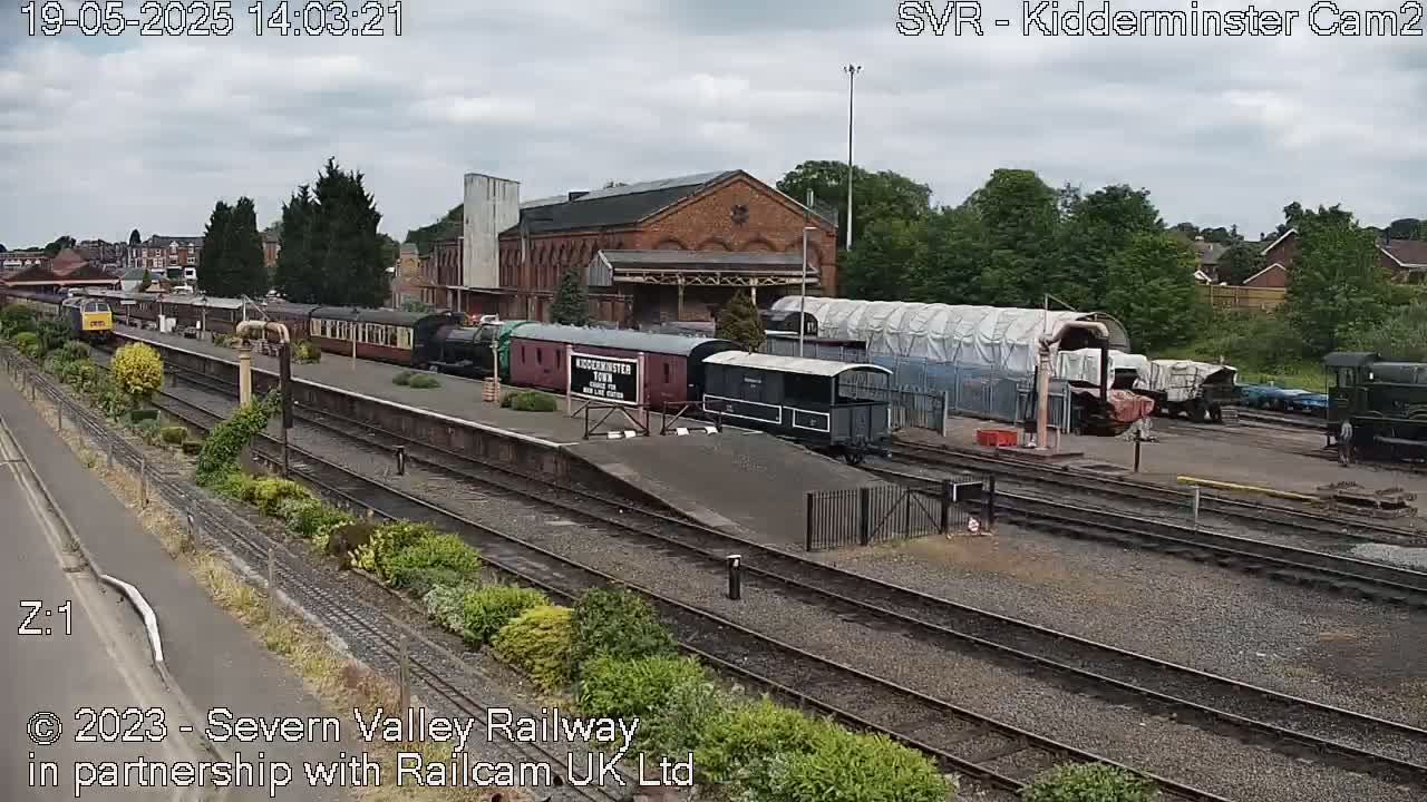 A train station with several rail cars and a brick building is seen under an overcast sky.