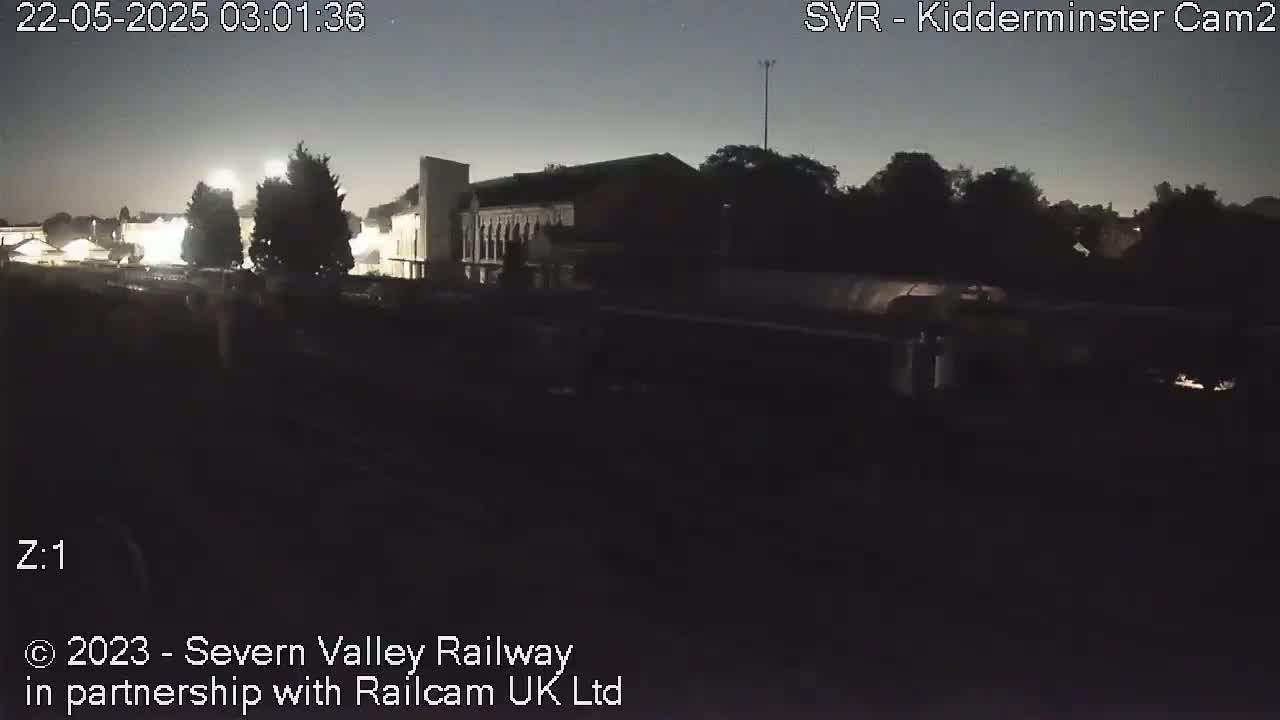 A nighttime, low-light view of a building and trees near a railway line.