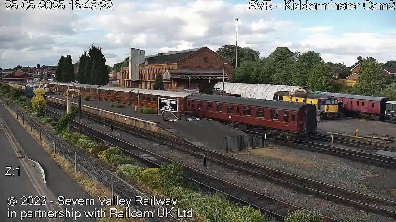 A mostly cloudy day at a train station shows several railway cars and locomotives on various tracks.