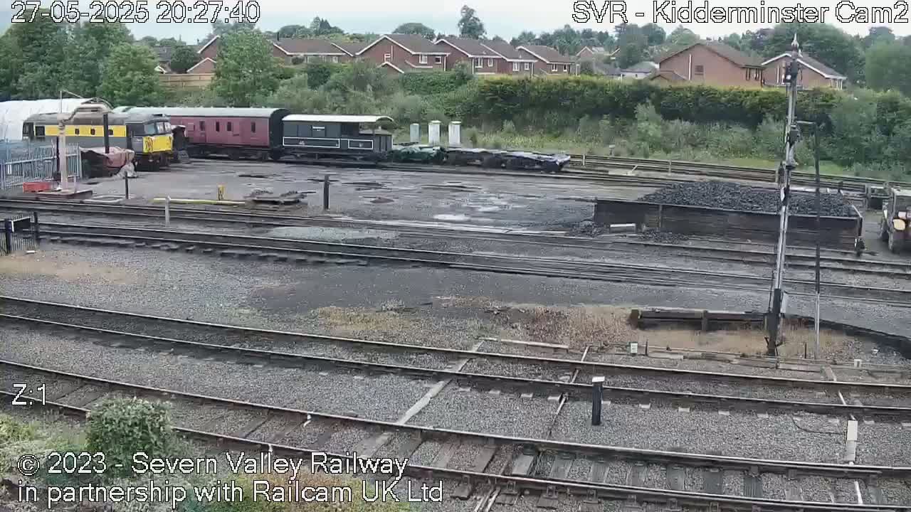 Several diesel locomotives and railway cars are parked in a rail yard on an overcast evening.
