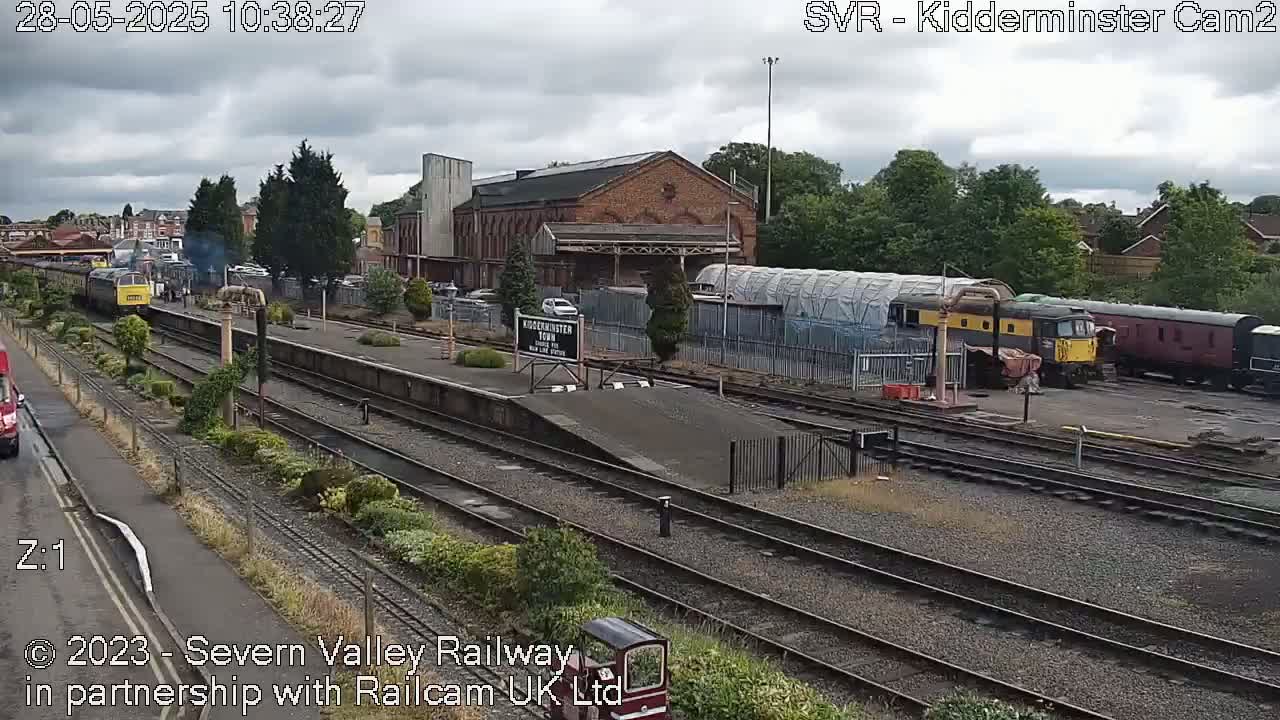 A train station with multiple train cars and a brick building under an overcast sky.