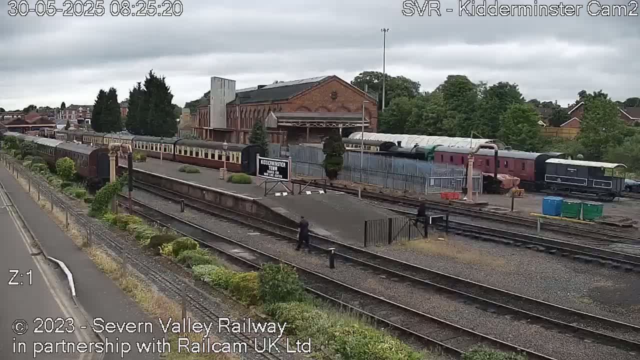 A train station with several passenger cars and locomotives on the tracks under an overcast sky.