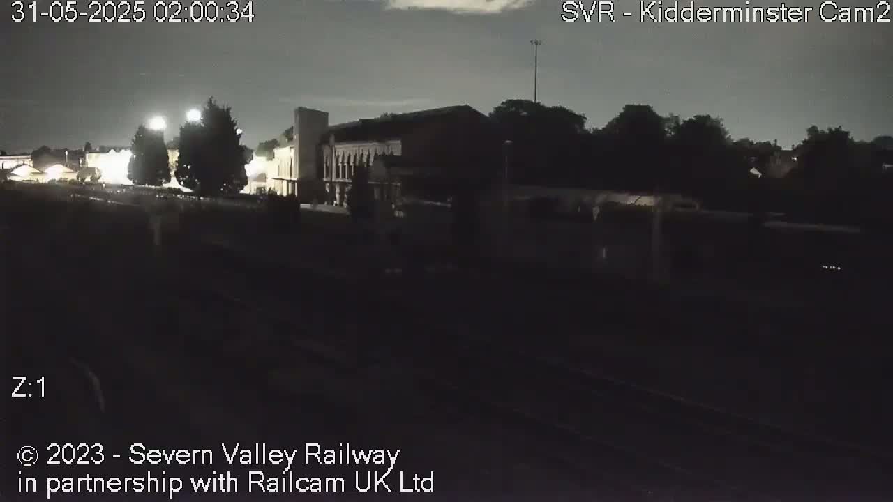 A nighttime view of a train station with a large building and trees under a dark sky.
