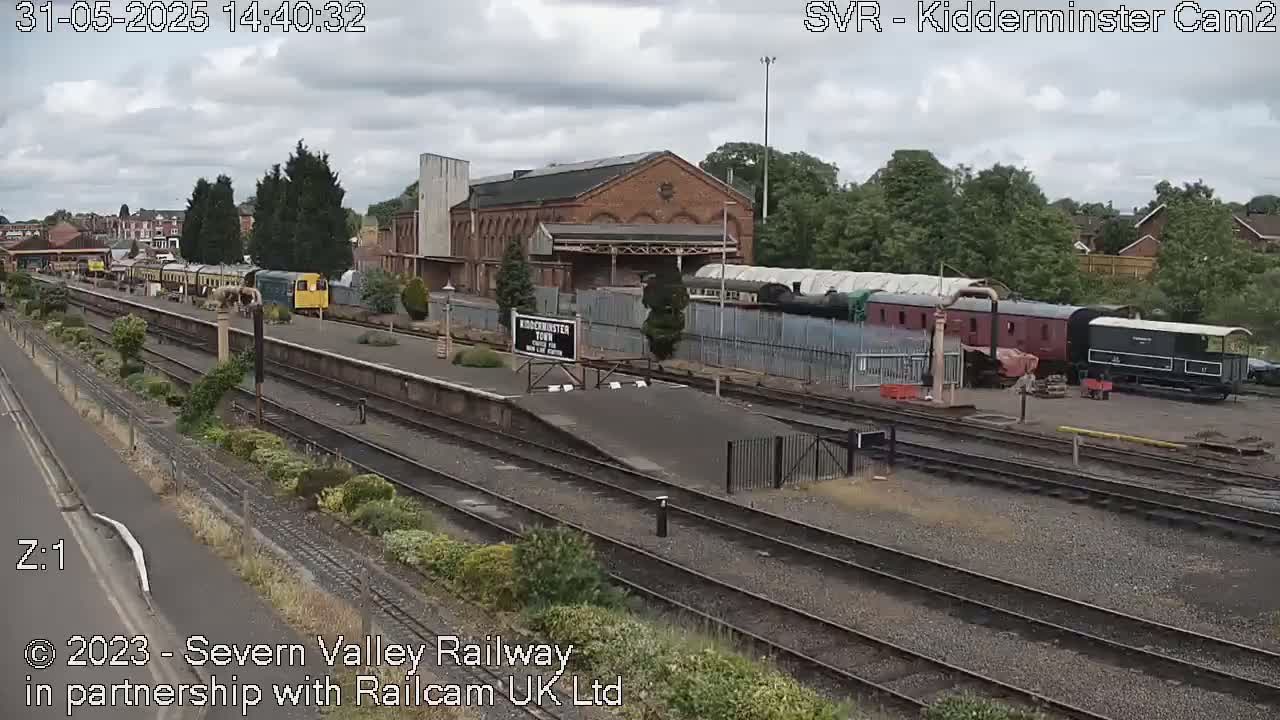 A train station on a partly cloudy day with multiple train cars and a brick building visible.