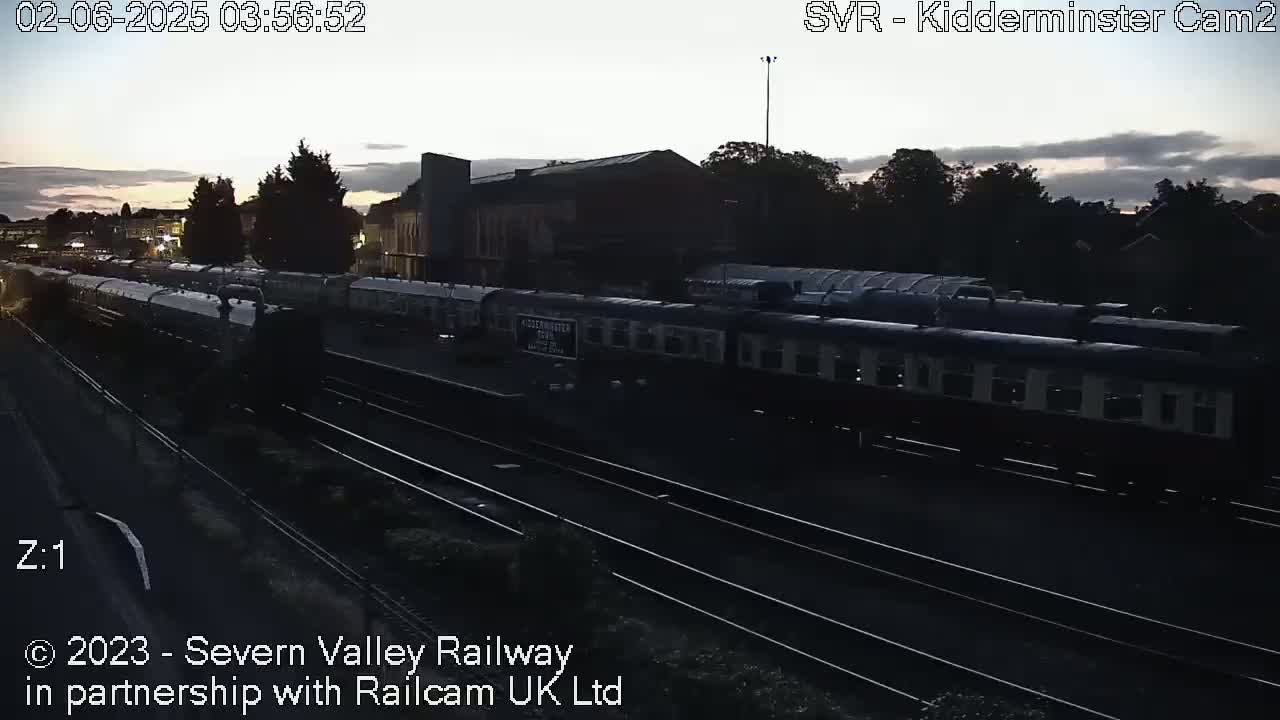 A long passenger train sits at a station during twilight.
