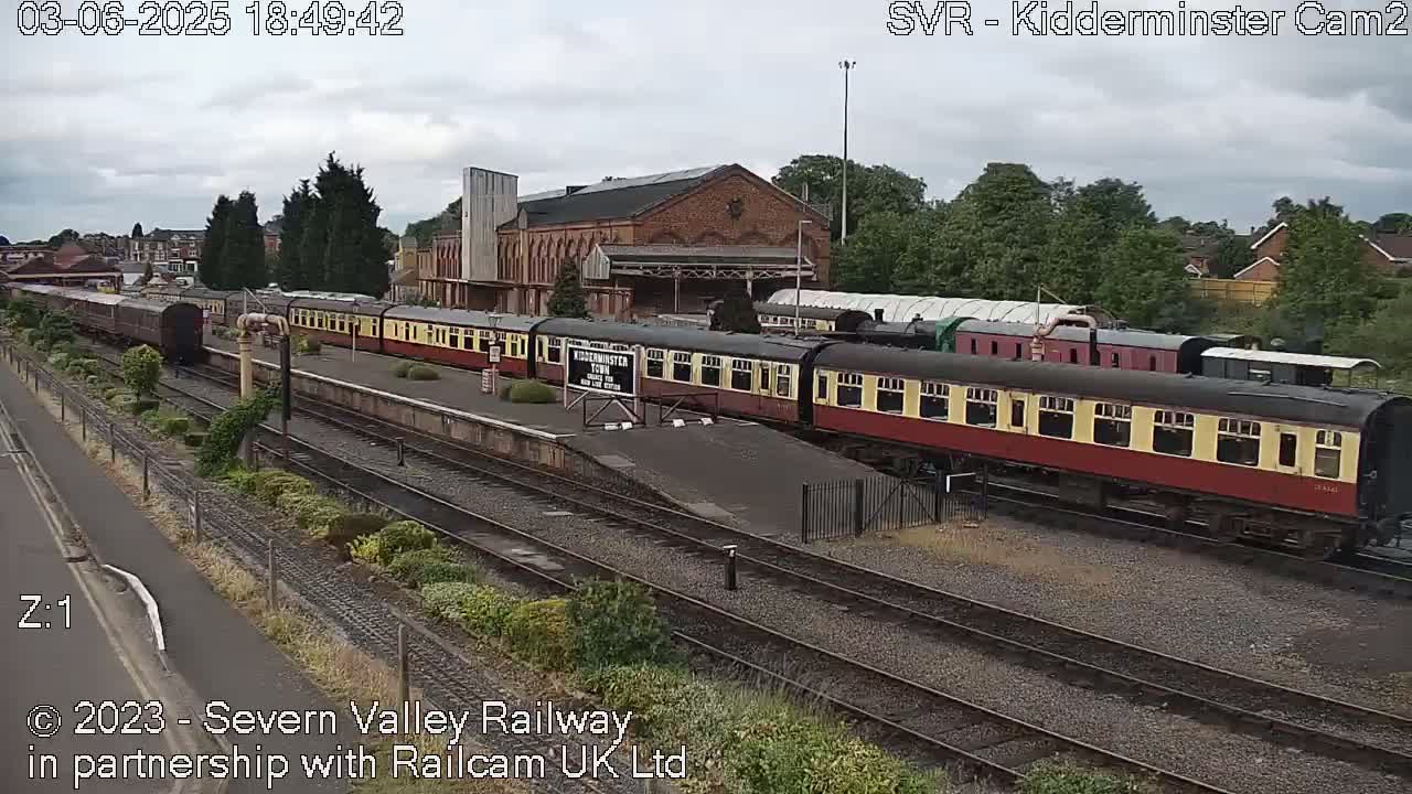 A long train of red and cream passenger cars sits at a station on an overcast day.