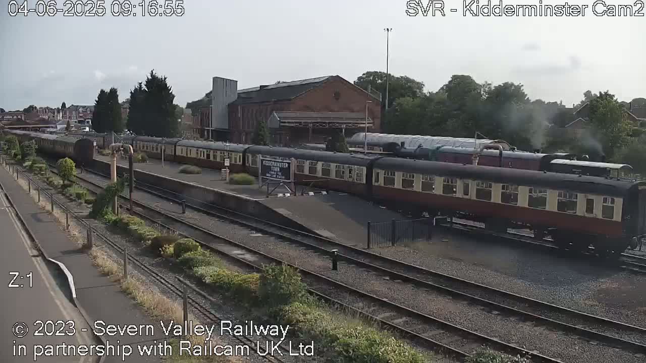A long train of vintage passenger cars sits at a station on a partly cloudy day.