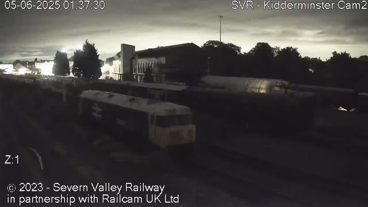 A nighttime, dimly lit view of a train in a station, under a cloudy sky.