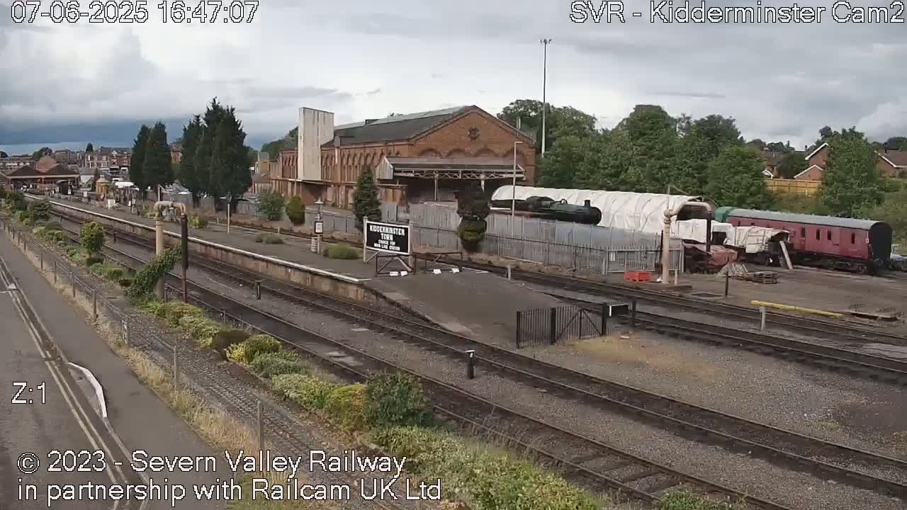 A train station with multiple train tracks, a brick building, and several train cars under an overcast sky.