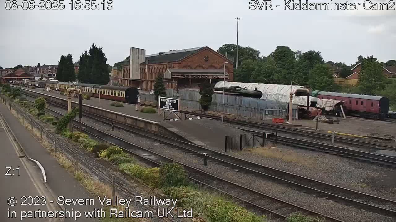 A railway station with several train cars and a large brick building under an overcast sky.
