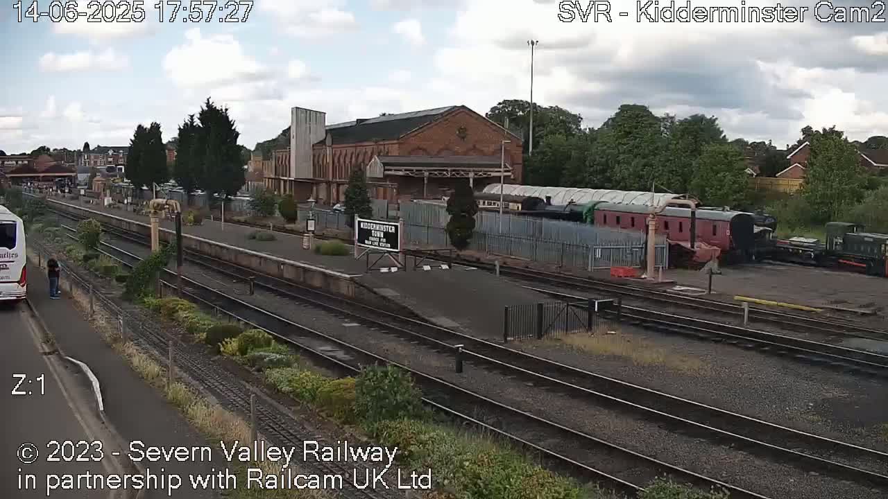 A train station with multiple train cars and a bus, under a partly cloudy sky.