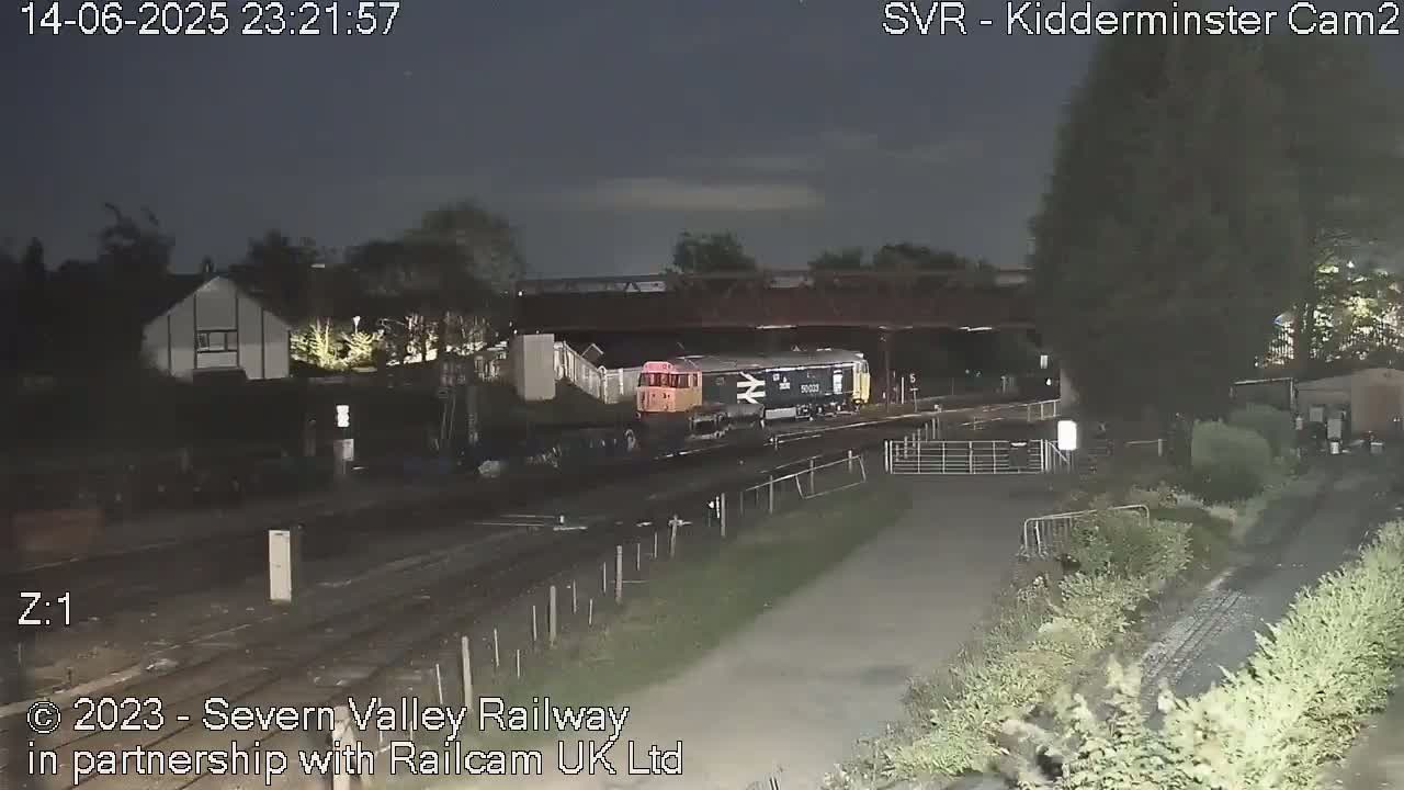 A train station with multiple train cars and a bus, under a partly cloudy sky.