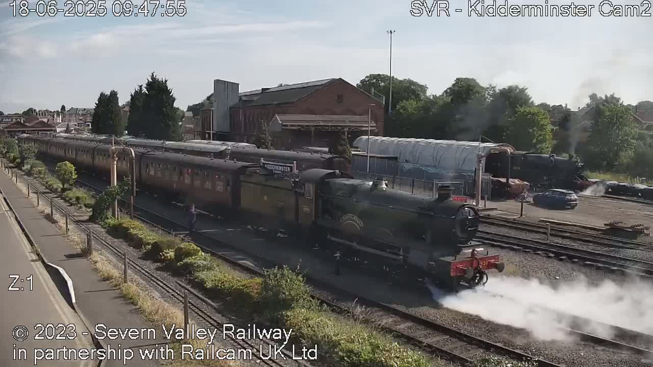 A steam train pulls a long line of passenger cars along train tracks on a sunny day.
