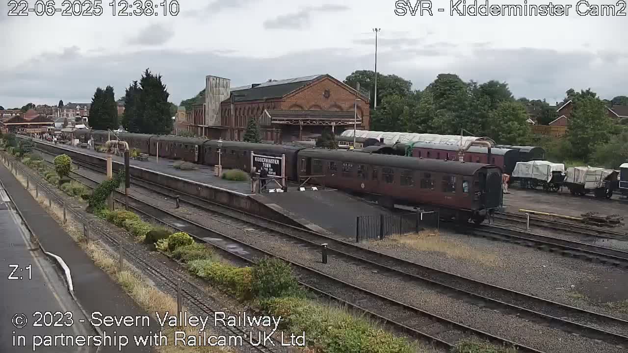A train station on an overcast day with multiple passenger cars and rail cars parked on various tracks, some covered and others uncovered.