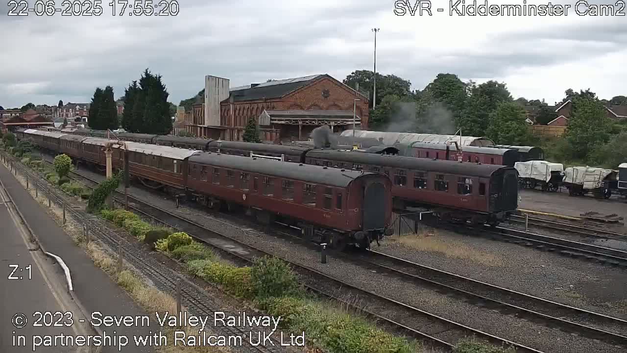 A long maroon train sits in a train yard on an overcast day.