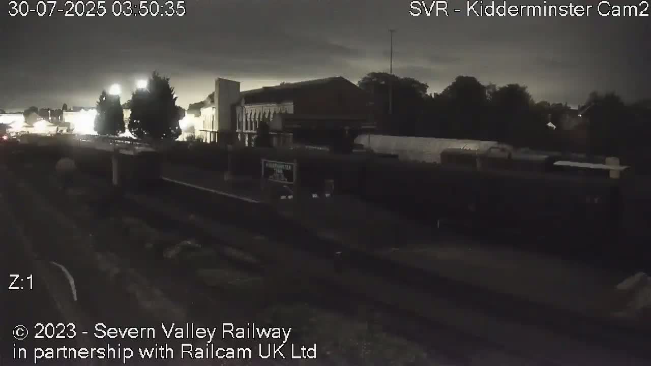 A brown wooden passenger railcar sits on train tracks in a rail yard on an overcast day.