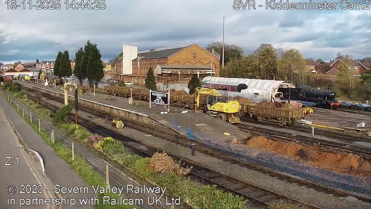 A nighttime, low-light view of a dark train and buildings partially obscured by trees under an overcast sky.
